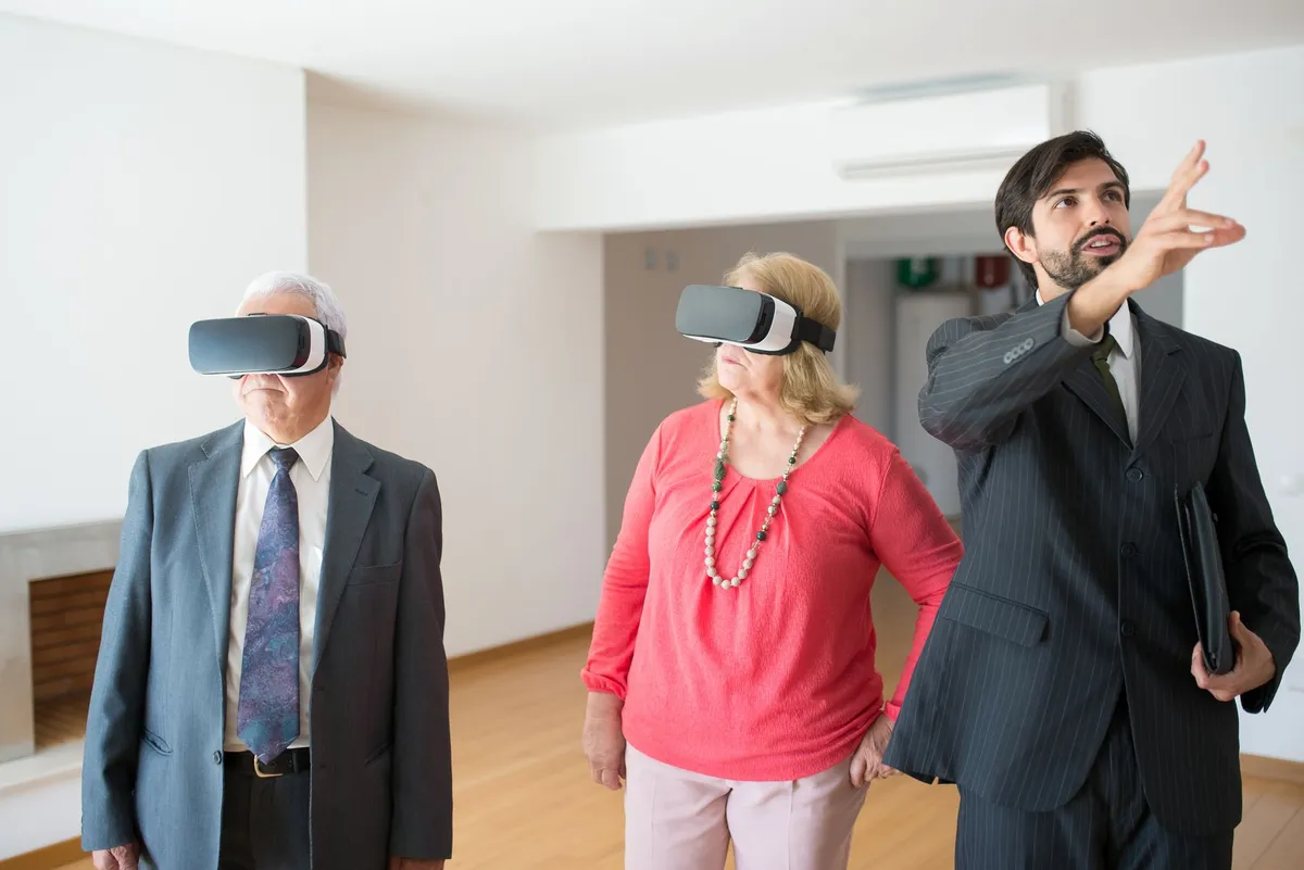 Un couple de seniors coiffé de casques de réalité virtuelle, guidé par un agent dans un appartement vide